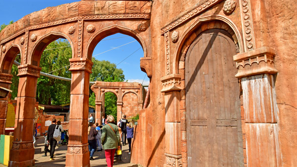 A view of intricately designed arched doorways and structures in a vibrant outdoor setting, with visitors walking nearby, showcasing the architectural beauty of the area.