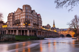 historic building along a river in Bath at dusk, showcasing elegant architecture with soft lighting and reflections in the water