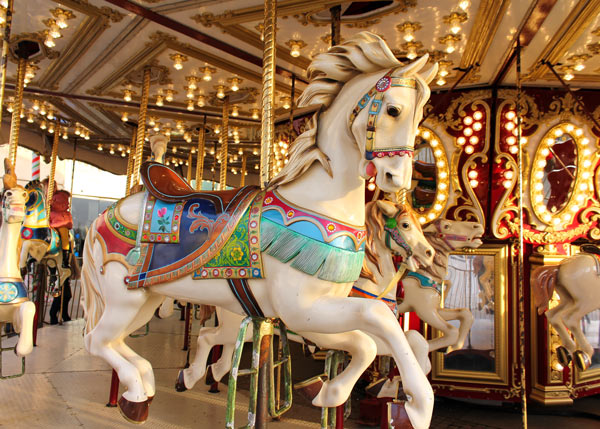 A beautifully painted carousel horse with intricate details, surrounded by other carousel horses, set against a backdrop of bright lights. Ideal for showcasing vintage carousel art.